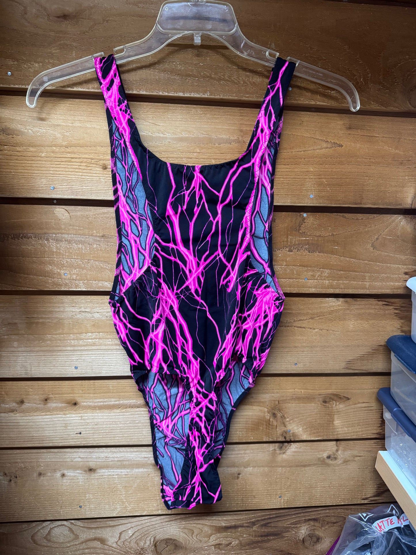 Back view of a neon pink and black men’s thong bodysuit displayed on a clear hanger.