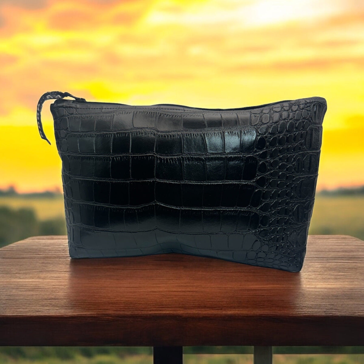 Handmade black faux crocodile makeup and travel pouch standing upright on a wooden table against a colorful yellow-orange background.