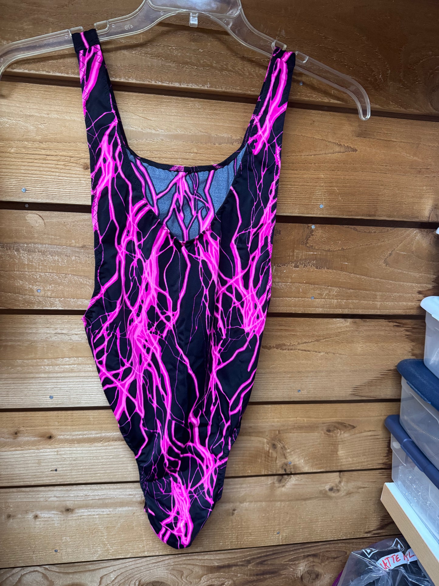     Front view of a neon pink lightning-print men’s bodysuit displayed on a clear hanger.
