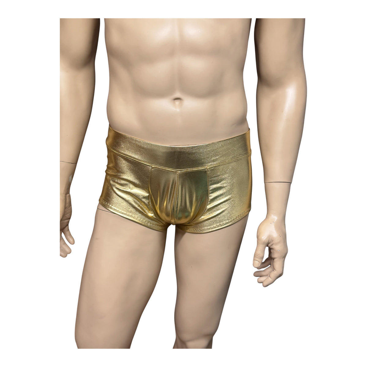 Men's shiny gold booty shorts on a mannequin against white, showing the front pouch, wide waistband, and fitted cut.