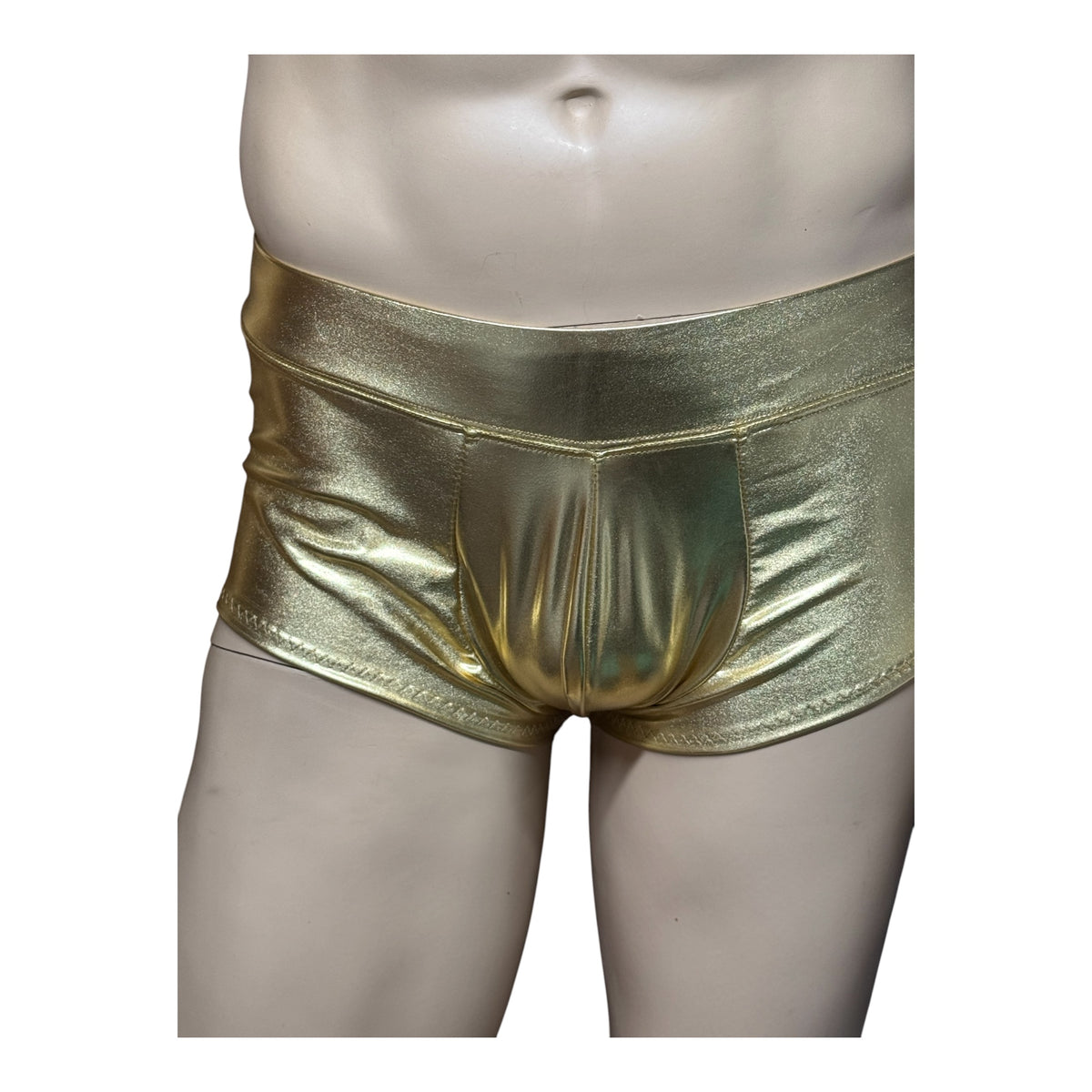 Close-up front view of shiny gold booty shorts on a mannequin, showing the wide waistband and shaped front pouch.
